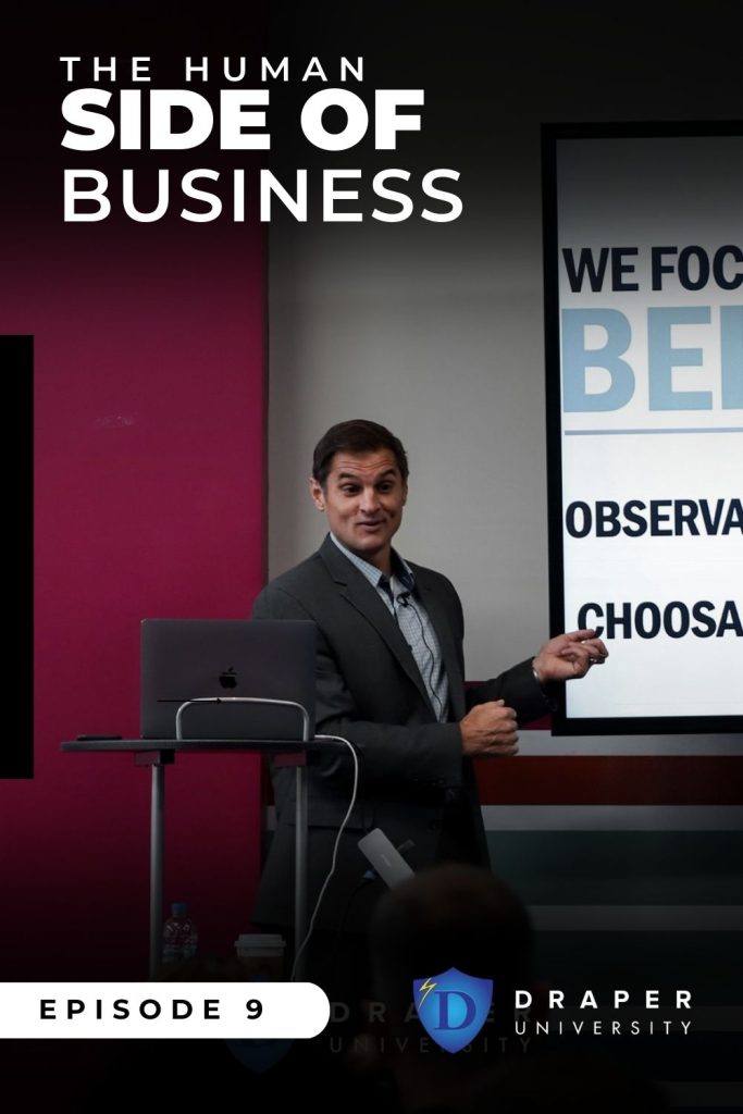 " The Human Side of Business " text sits overhead of a speaker behind a podium making a presentation.